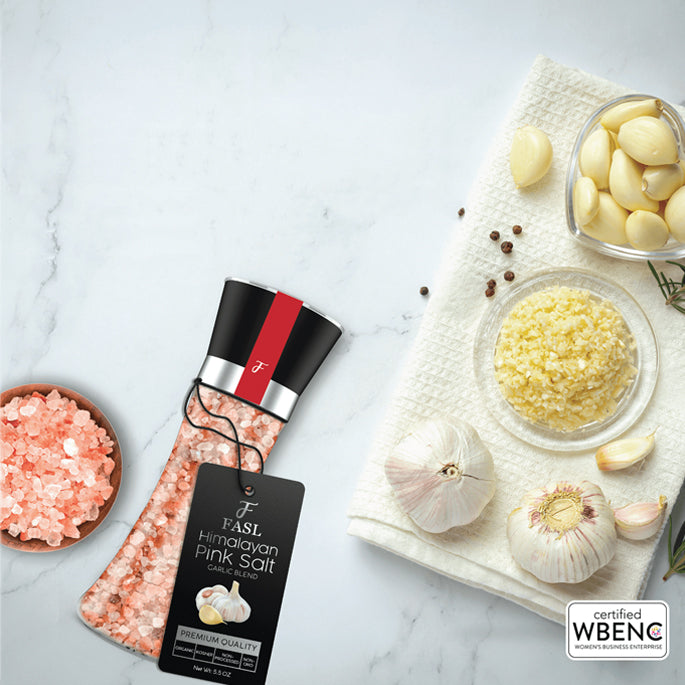 FASL Himalayan pink salt garlic blend in a marble table top along with whole garlic, garlic cloves and minced garlic.